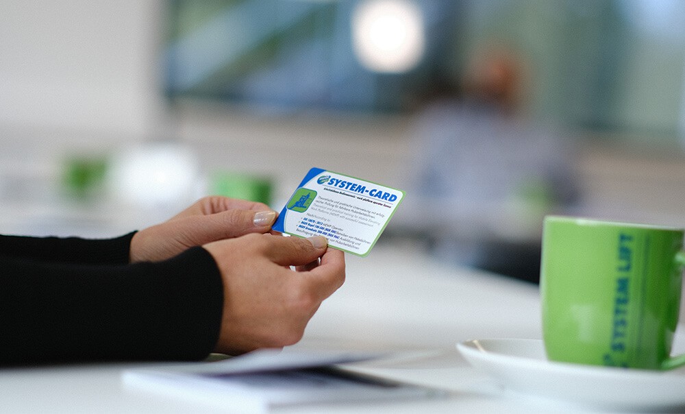 Eine Frau hält eine SYSTEM-CARD Arbeitsbühnen in den Händen.